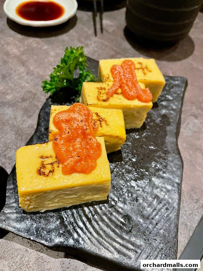 A close-up of tamagoyaki (rolled omelet) with a spicy topping and garnish.