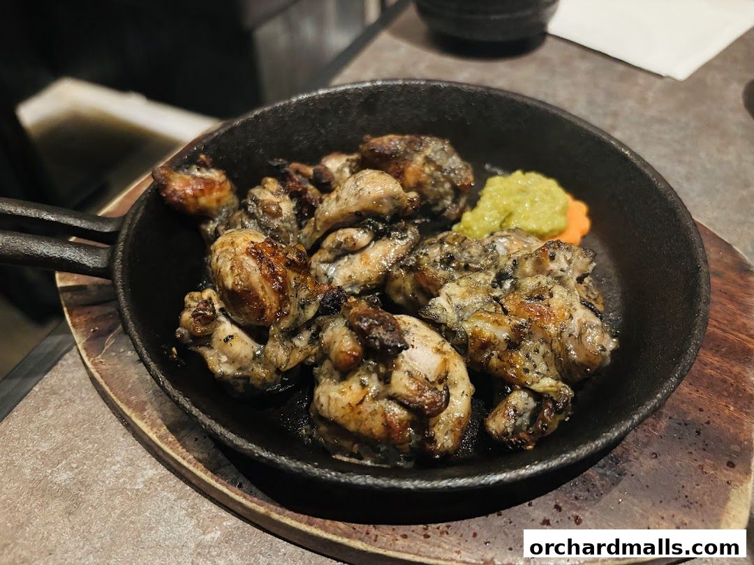 A close-up shot of grilled chicken pieces served in a cast-iron pan with a side of green paste.