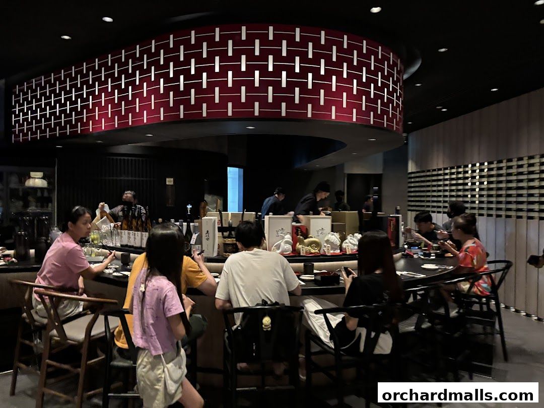 Diners seated at a sushi bar, with chefs preparing food behind the counter.