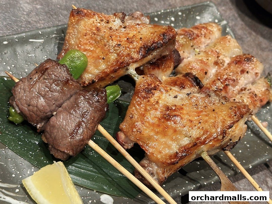 Close-up of grilled skewers with beef, chicken, and green peppers, served with a lemon wedge.