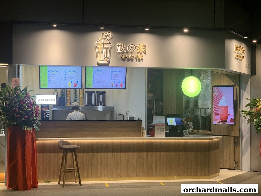 The exterior of a modern bubble tea shop called Qiu De Tea with illuminated menus.