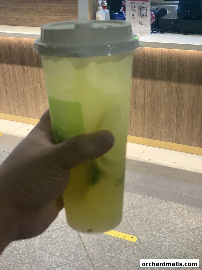 A hand holds a refreshing, pale green beverage in a clear plastic cup with a straw.