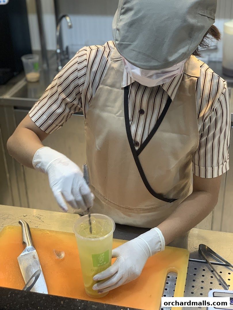 A barista prepares a refreshing drink with ice and fruit at a counter.