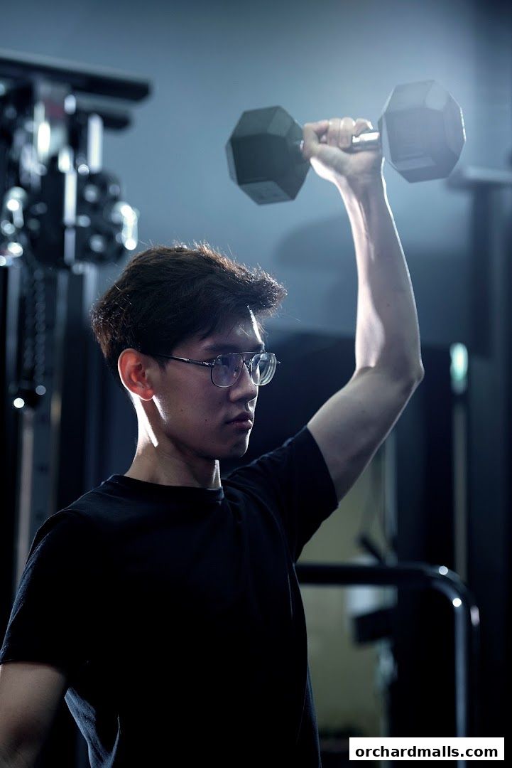 A man in glasses lifts a dumbbell in a gym setting.