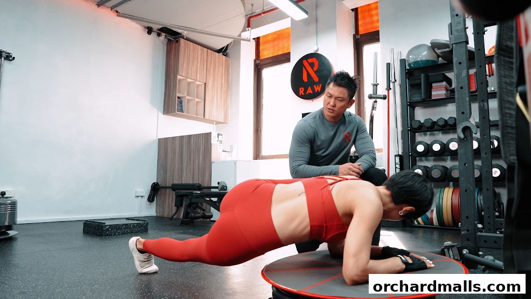 A personal trainer instructs a client performing a plank exercise in a gym.