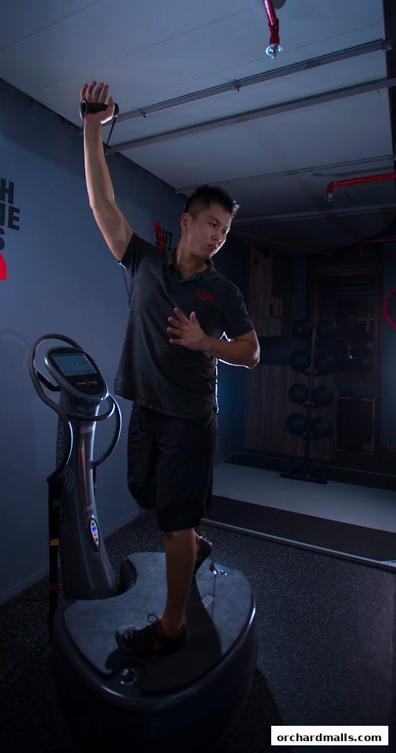 A man exercises on a vibration plate machine with resistance bands.