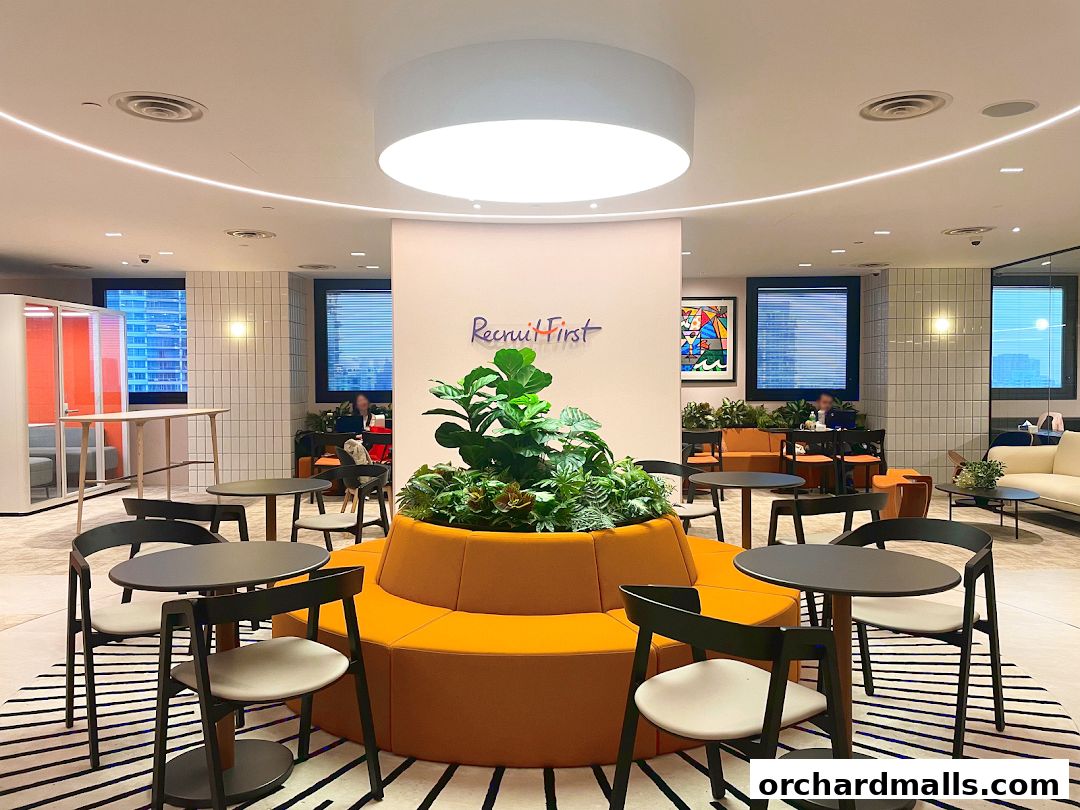 Modern office waiting area with seating, plants, and the RecruitFirst Singapore logo.