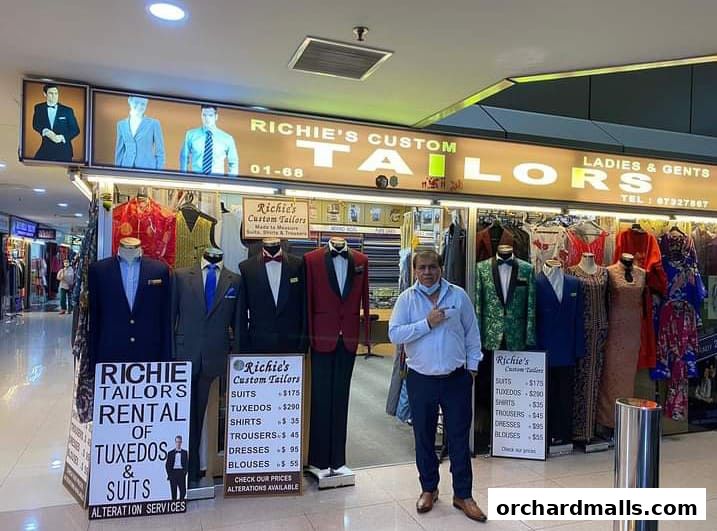 A tailor shop displaying suits, tuxedos, shirts, and dresses with price lists outside.