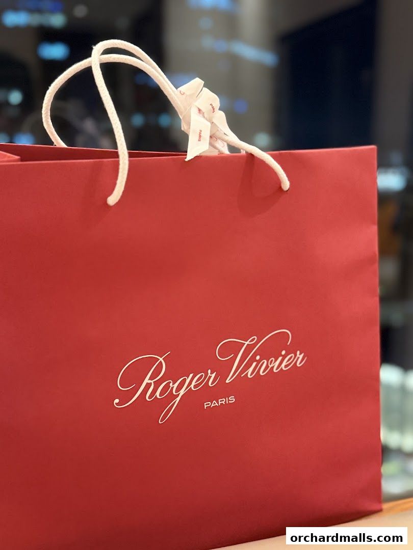 A red shopping bag from Roger Vivier with white rope handles and logo.
