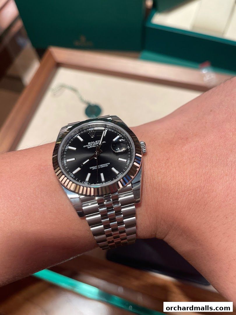 A close-up shot of a Rolex watch on a wrist, with a green Rolex box in the background.