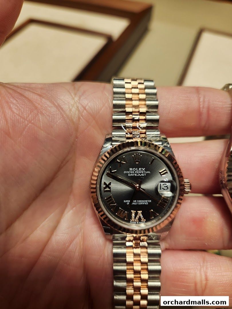 A hand holds a luxurious Rolex Datejust watch with a two-tone metal band.