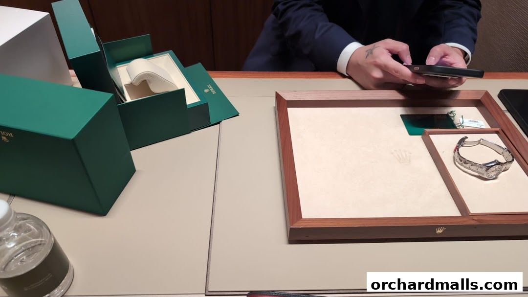 A Rolex watch is displayed in a wooden tray next to its green packaging.