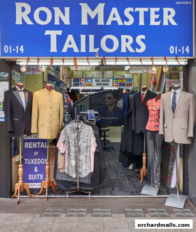 Shop front of Ron Master Tailors displaying suits, tuxedos, and shirts on mannequins.