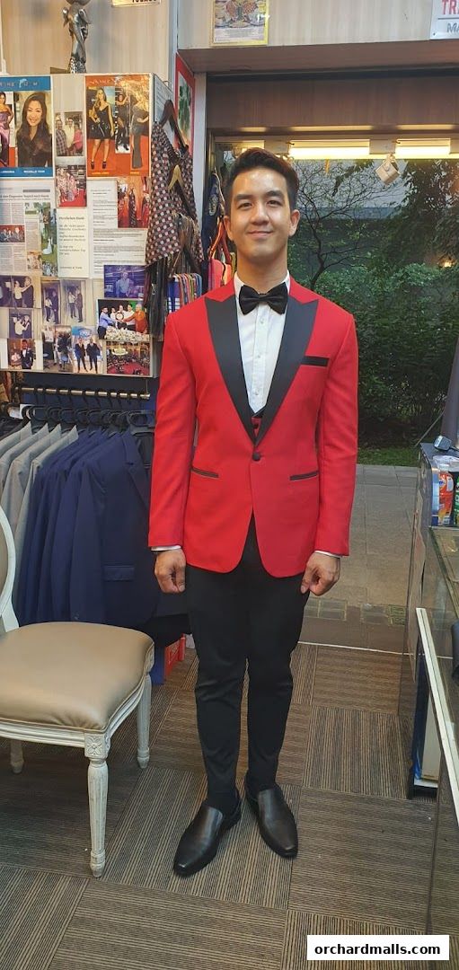 A man models a striking red tuxedo with black lapels at a tailor shop.