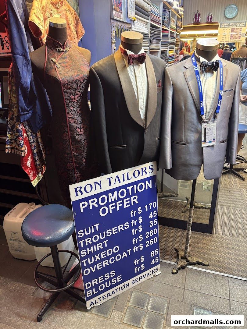 Mannequins display formal wear and traditional attire outside Ron Tailors with a promotion sign.