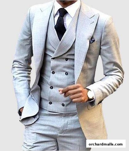 A man wearing a light grey three-piece suit with a black tie and watch.