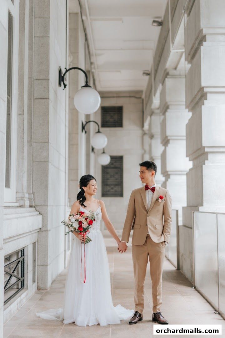 A bride and groom holding hands, posing for a photo in a covered walkway.