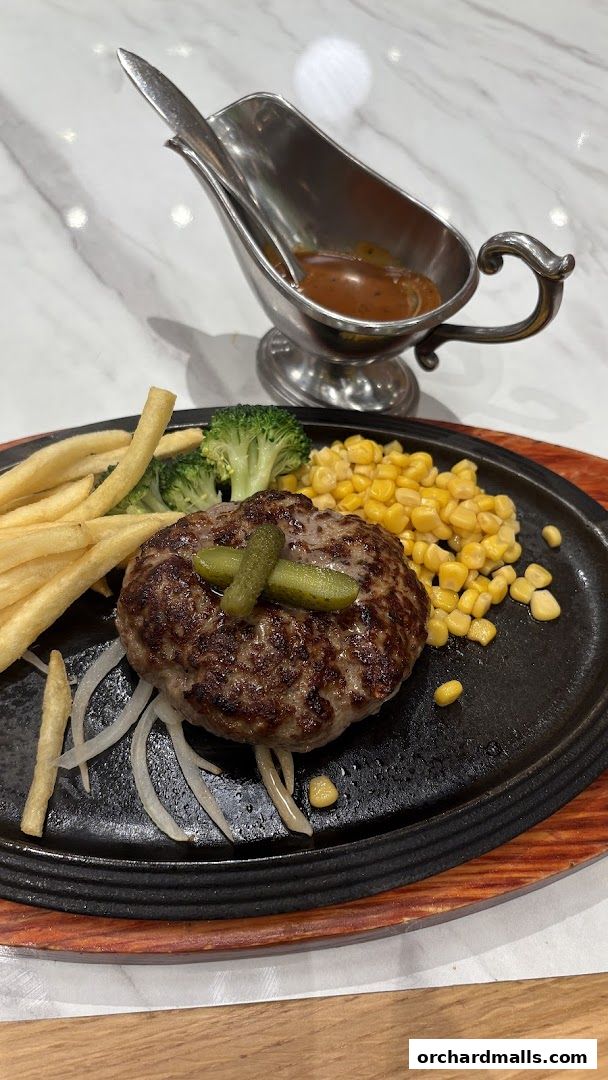 A sizzling hamburger steak served with fries, corn, broccoli, and gravy.