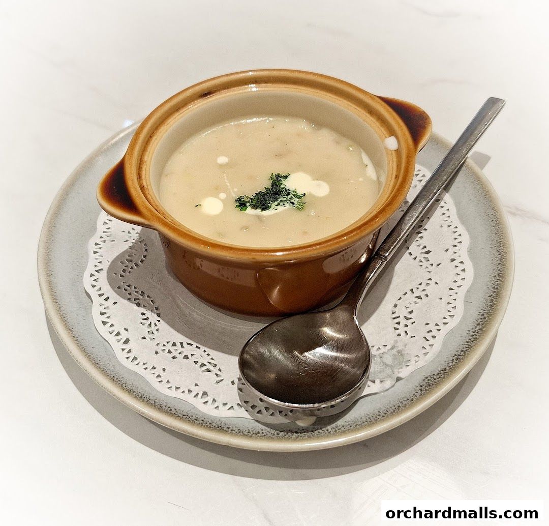 A close-up of a creamy soup served in a small brown pot with a spoon.