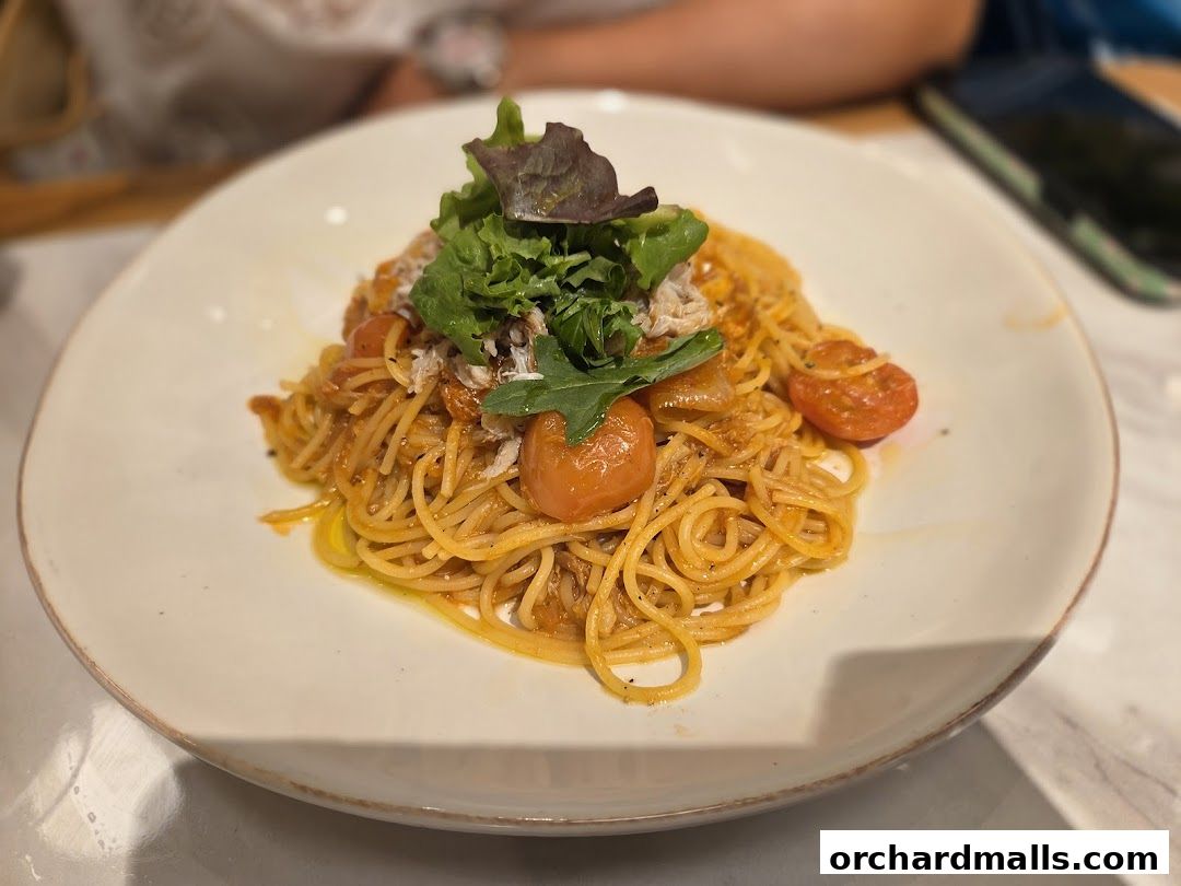 A plate of spaghetti with cherry tomatoes and greens, garnished with shredded meat.
