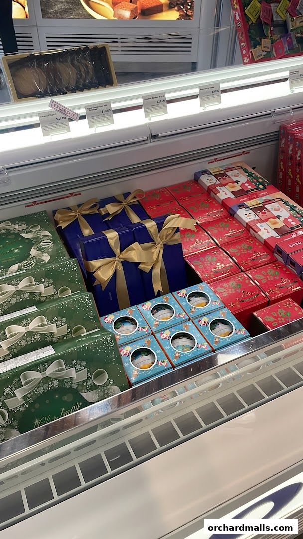 A display of festive holiday gift boxes and treats in a refrigerated case.