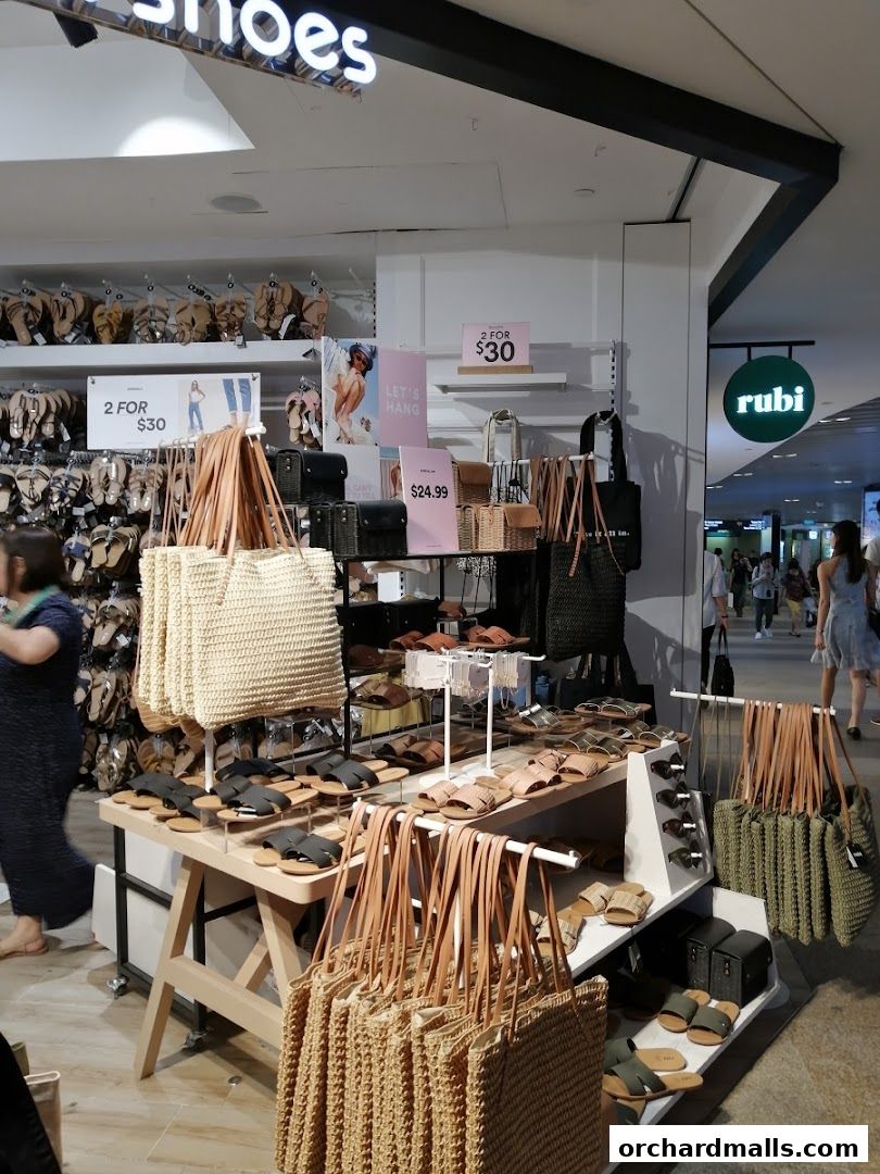 A Rubi Shoes store interior displaying sandals and woven bags with promotional signage.