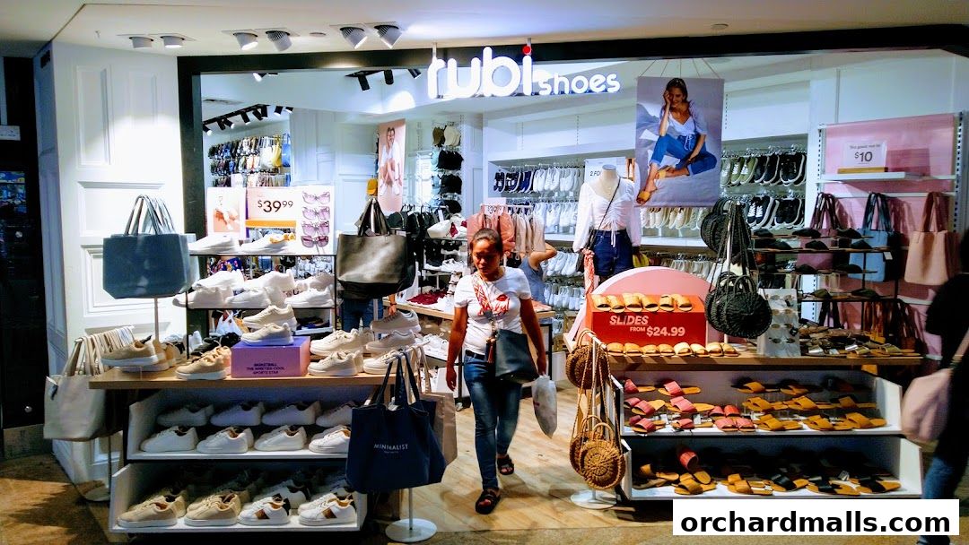 A well-lit shoe store displaying a variety of sneakers, slides, and handbags.