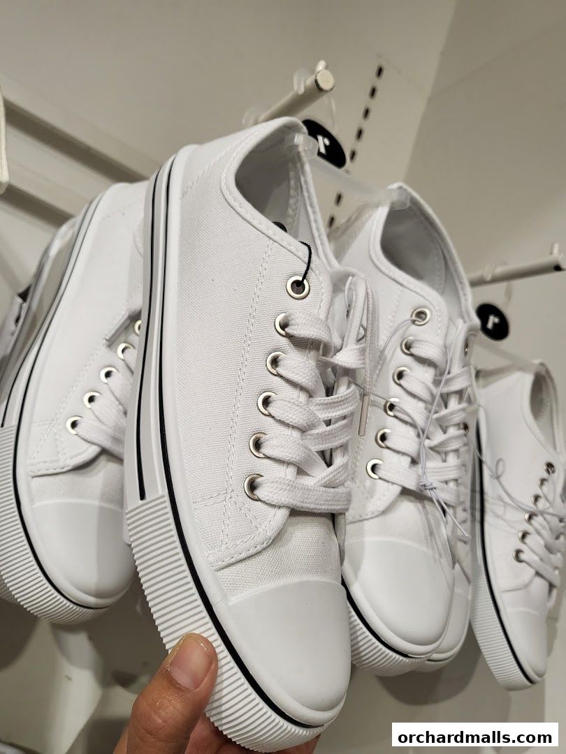 A close-up shot of several white canvas sneakers with black trim, displayed on a rack.