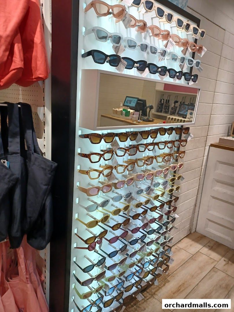 A wall display of various sunglasses in different styles and colors, with bags and clothing on the left.
