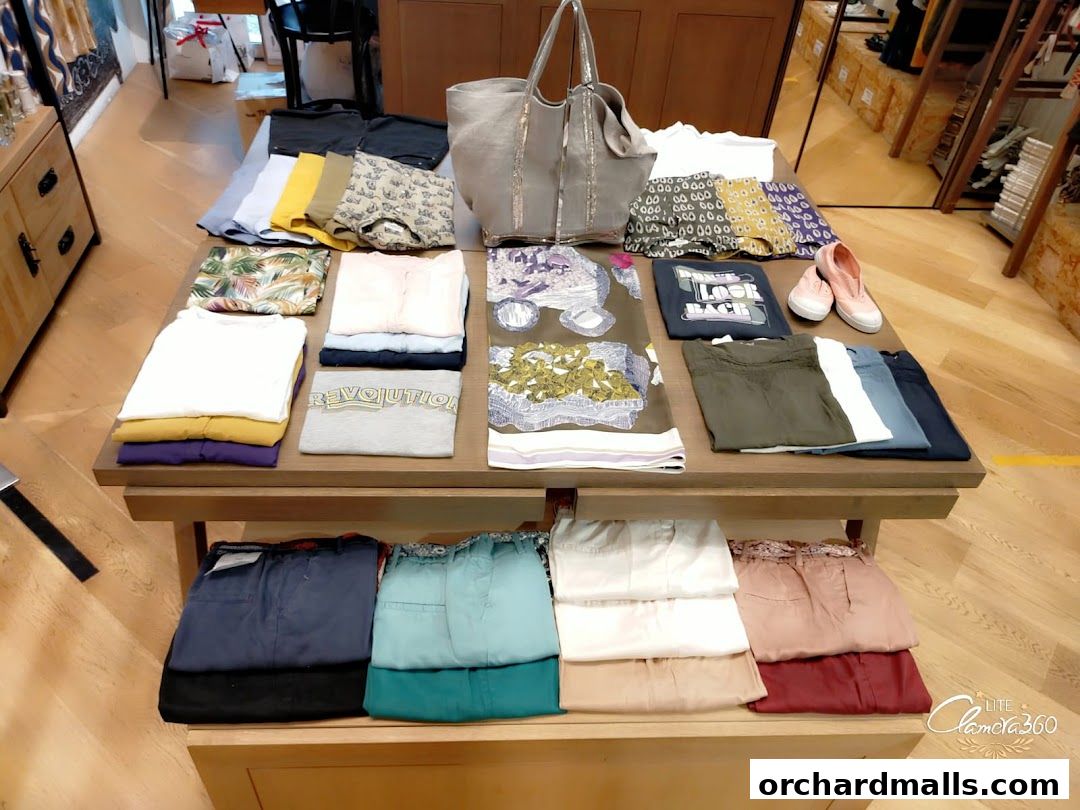 Neatly folded clothing and accessories displayed on a wooden table in a retail store.