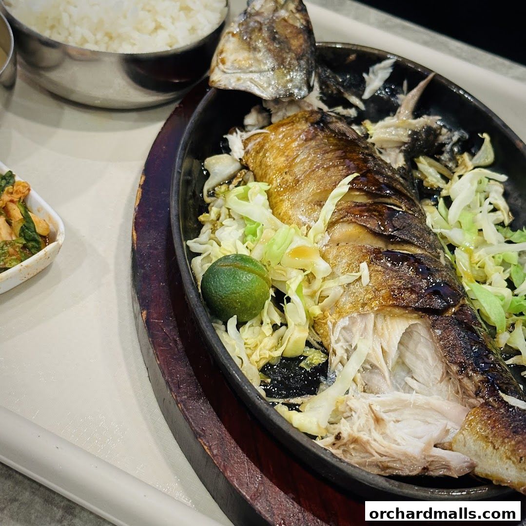 A sizzling grilled fish dish served with shredded cabbage and a lime wedge.