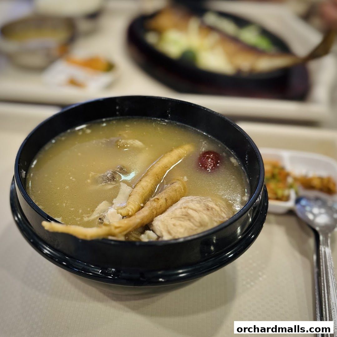 A close-up of a steaming bowl of Korean ginseng chicken soup with a side dish.