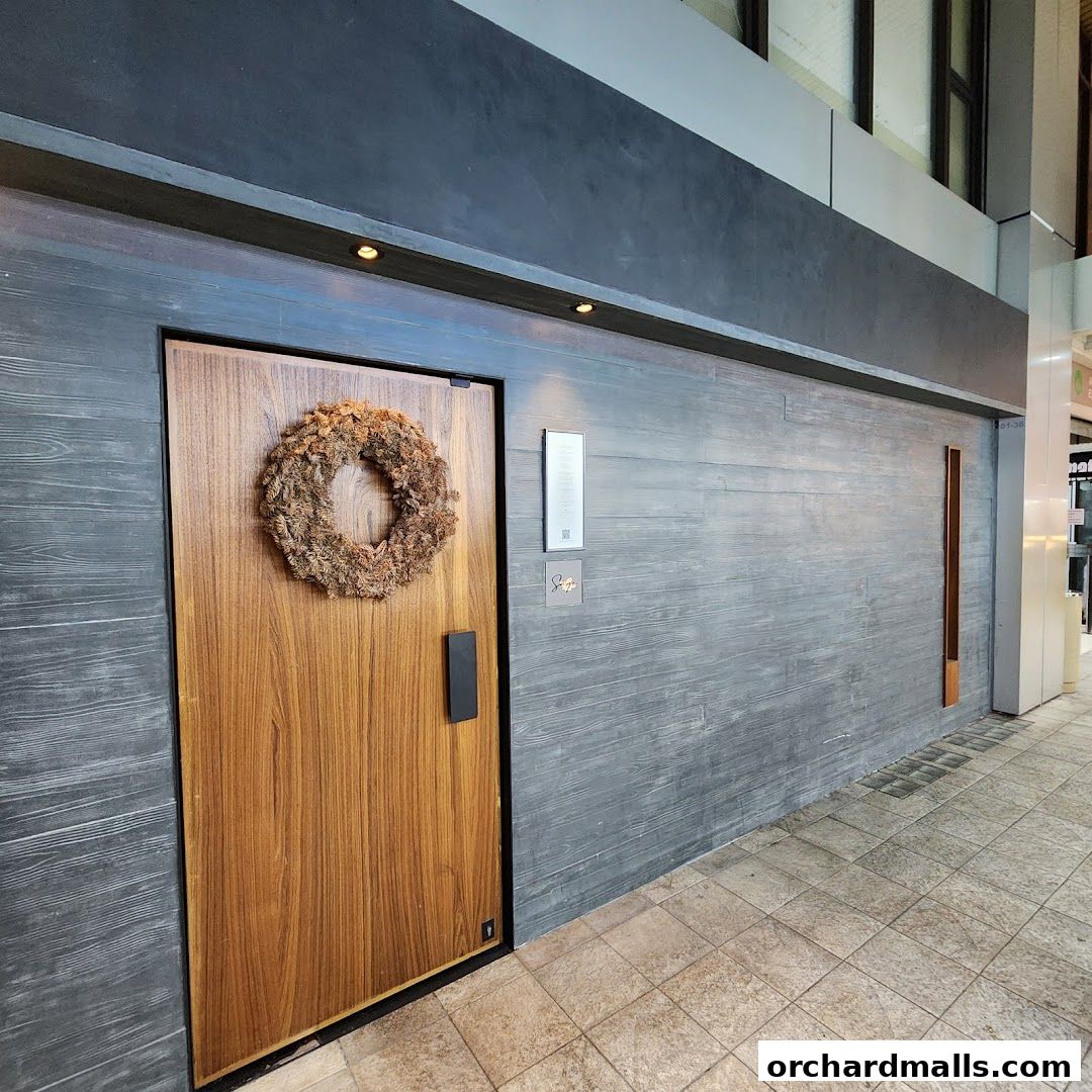 The entrance to Sage by Yasunori Doi features a wooden door with a wreath and modern grey paneling.