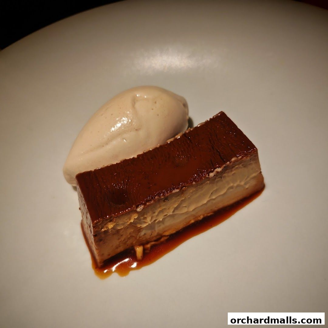 A rectangular slice of chocolate dessert with a scoop of ice cream on a white plate.
