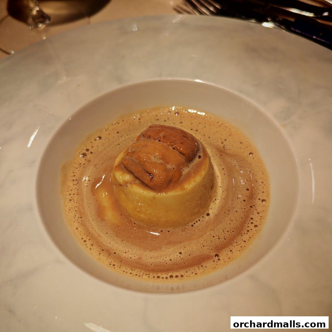 A close-up of a gourmet dish with sea urchin on top of a cylindrical food item in a creamy sauce.