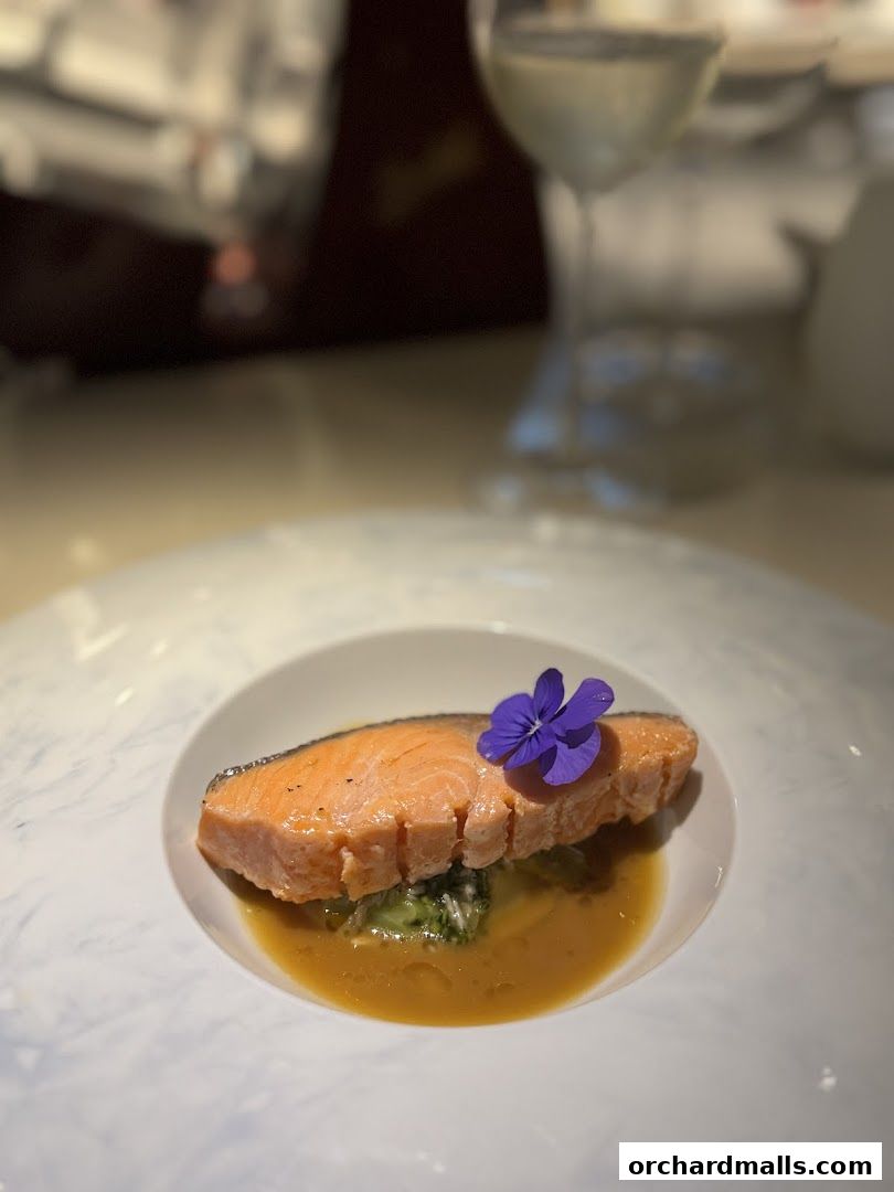 A beautifully plated salmon dish with a purple flower garnish and a glass of white wine.
