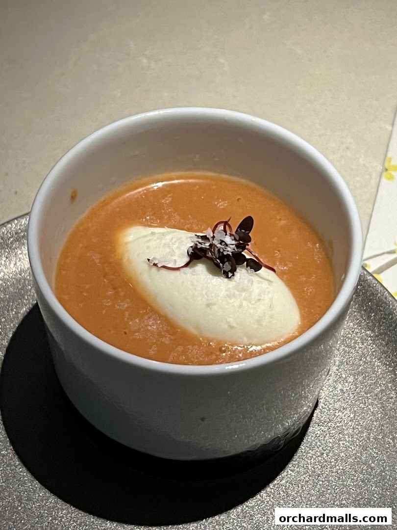 A bowl of creamy tomato soup topped with a dollop of white cream and microgreens.