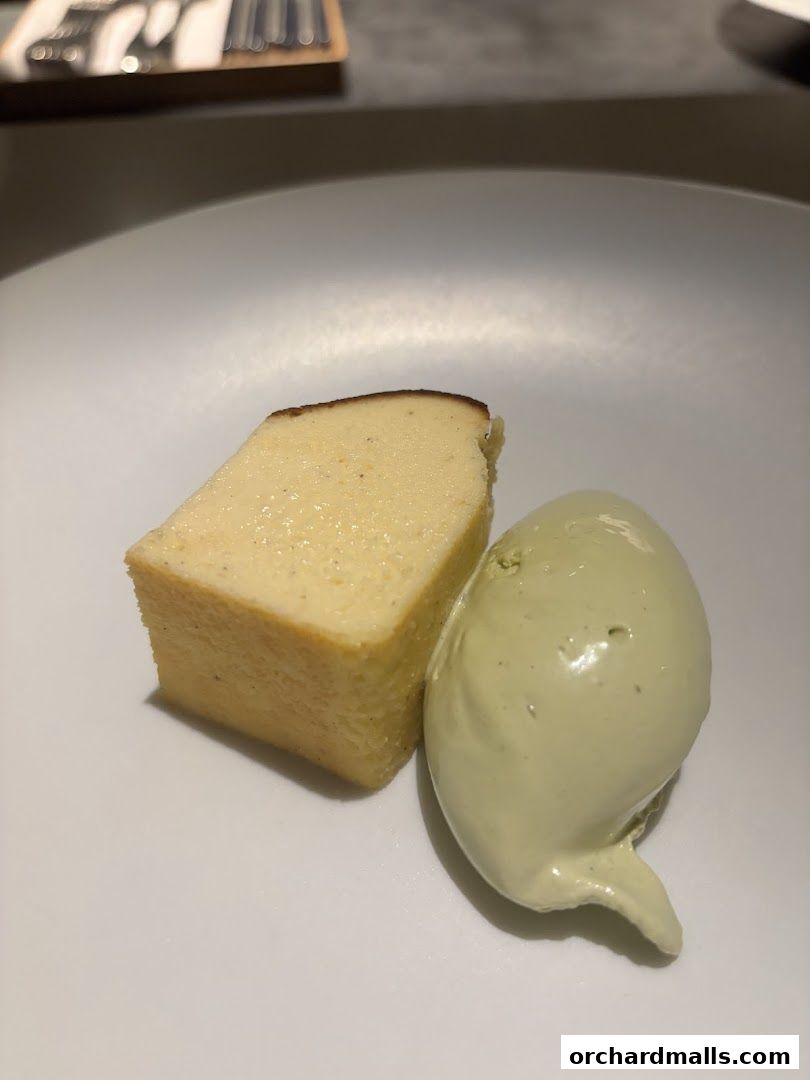 A slice of cheesecake with a scoop of green ice cream on a white plate.