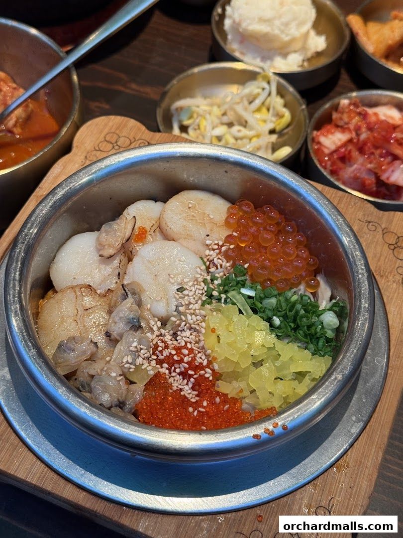 A close-up of a Korean pot rice dish with scallops, roe, and pickled vegetables.