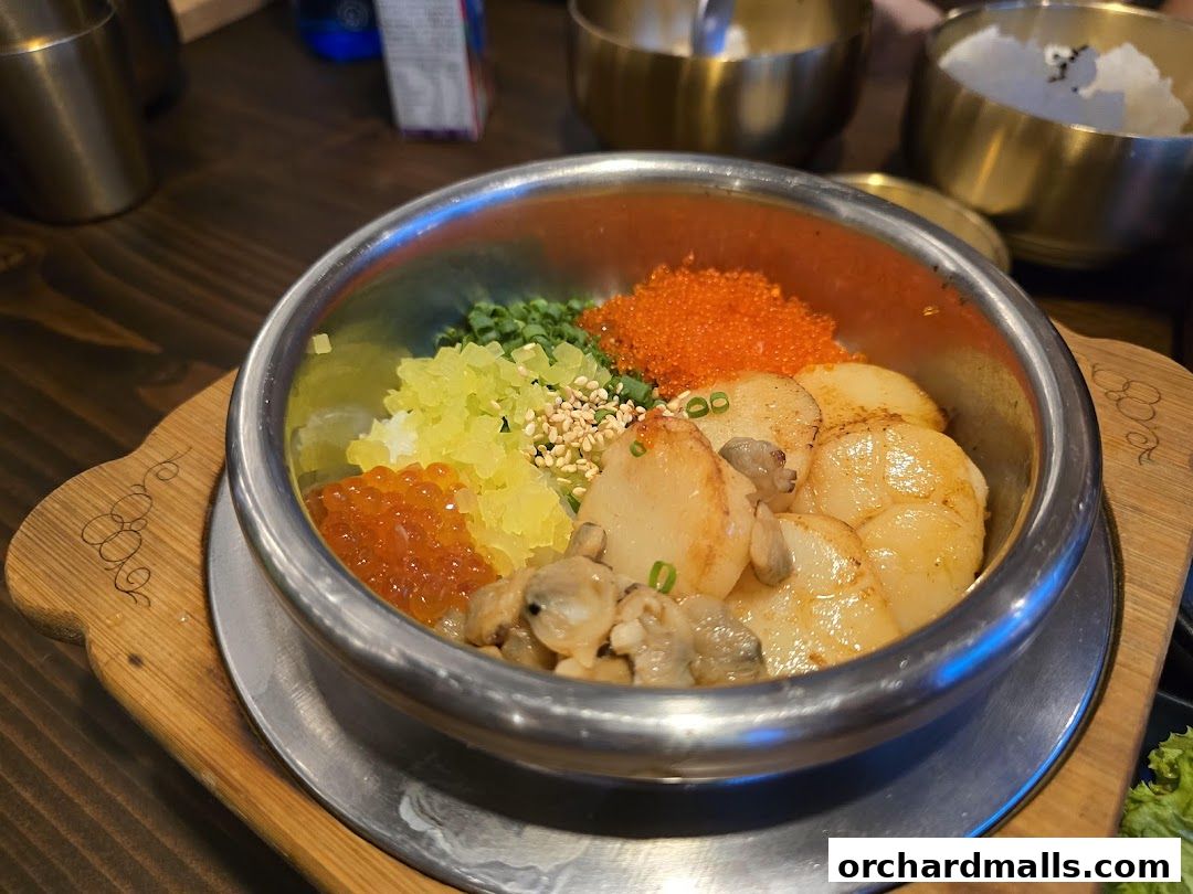 A close-up of a Korean pot rice dish with scallops, roe, and vegetables.