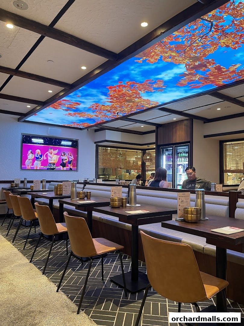 Interior of a Korean restaurant with tables, chairs, and a screen displaying K-pop.
