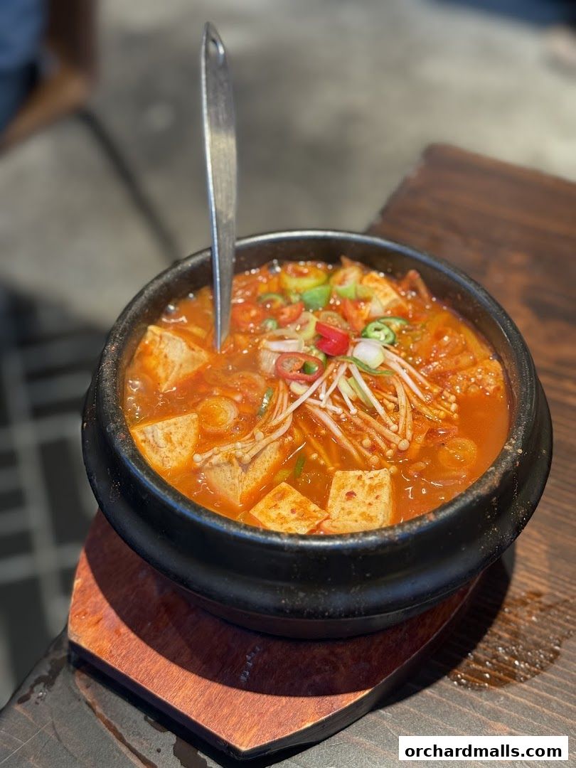 A steaming bowl of Korean kimchi stew with tofu and enoki mushrooms.