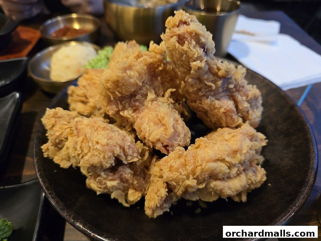 A close-up shot of crispy Korean fried chicken served on a black plate with side dishes.