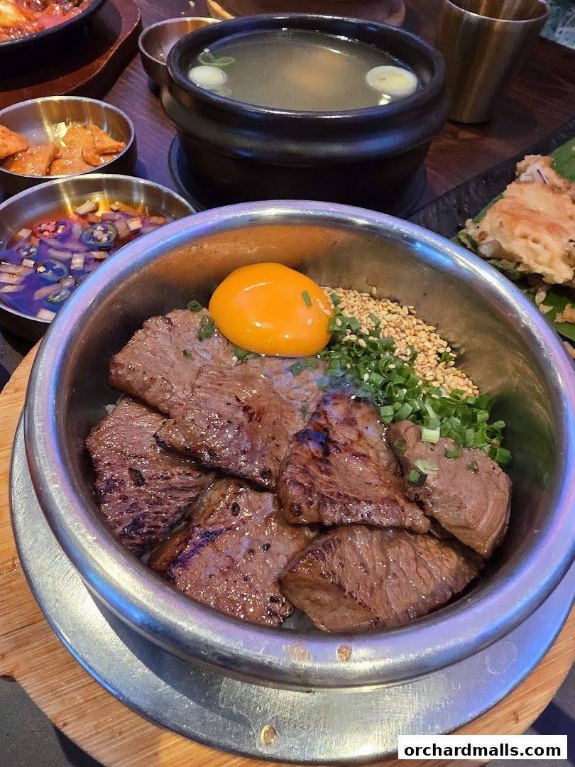 A close-up of a Korean pot rice dish with grilled beef and a raw egg yolk.