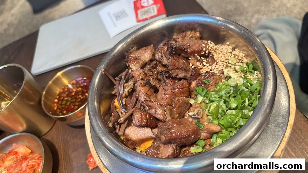 A close-up of a Korean pot rice dish with grilled meat and scallions.