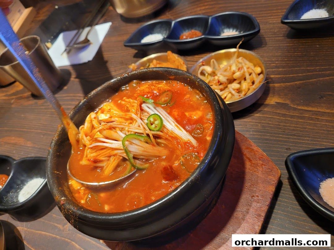 A close-up of a steaming Korean stew with tofu, mushrooms, and chili peppers.