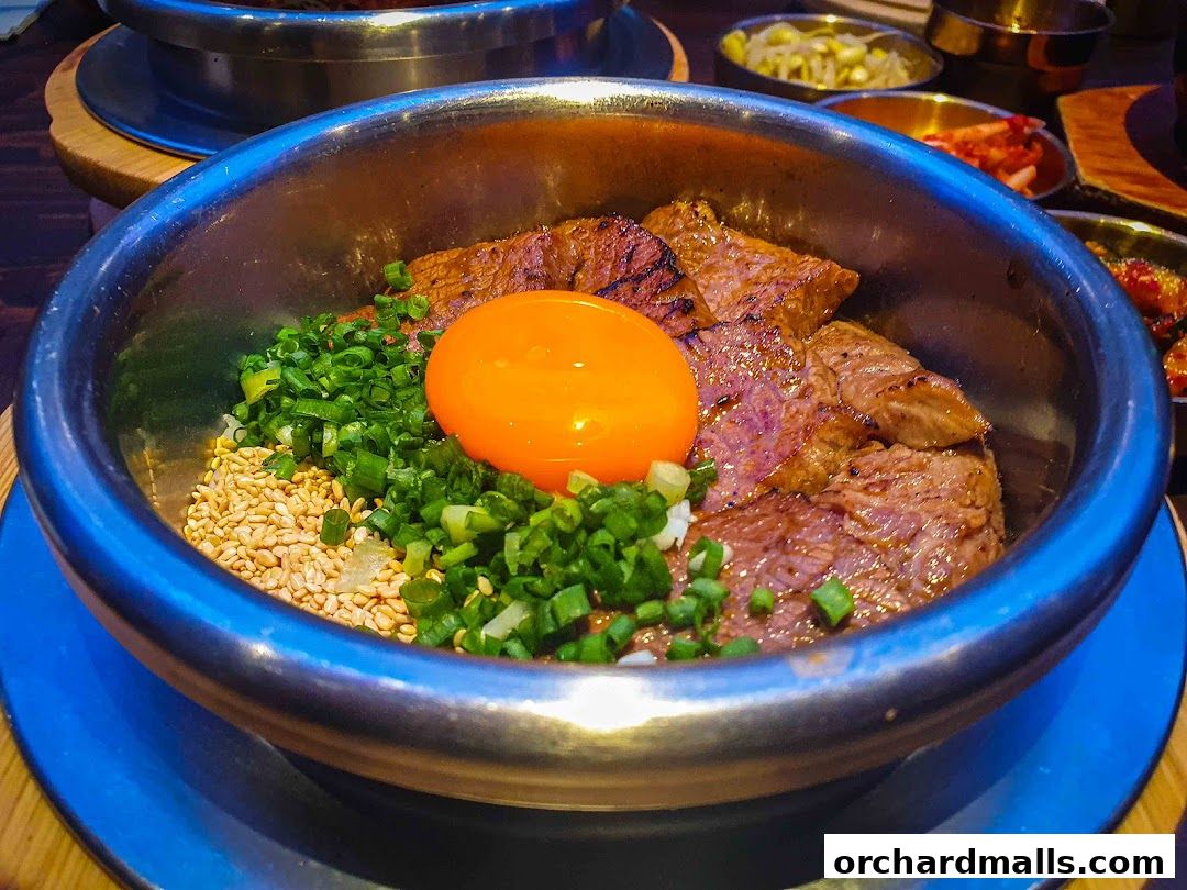 A close-up of a Korean pot rice dish with grilled beef, egg yolk, and scallions.