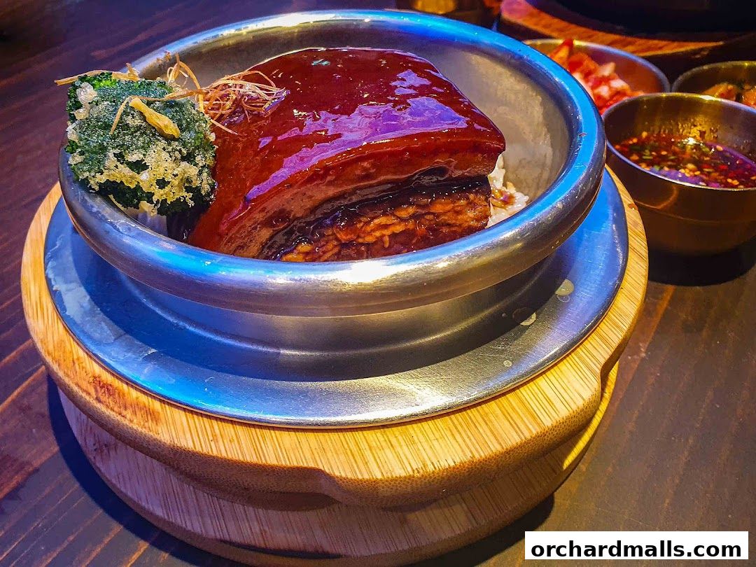 A close-up of a Korean pot rice dish with braised pork belly and a side of dipping sauce.