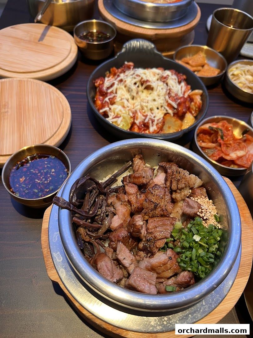 A close-up of a Korean pot rice dish with grilled meat and vegetables.