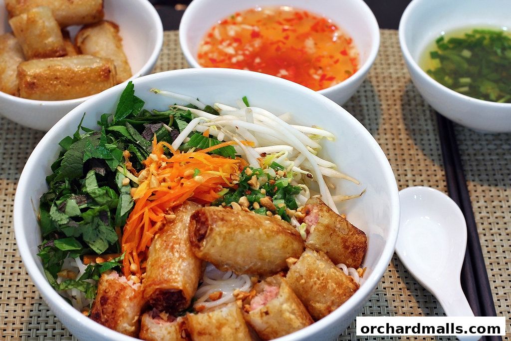 A close-up of a Vietnamese noodle dish with spring rolls, fresh herbs, and shredded carrots.